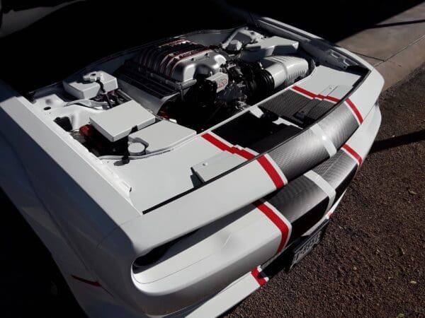 Car engine exposed with hood open, parked on roadside. White with red and black stripes visible on the front.