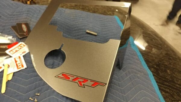 Close-up of a metal SRT panel on a table with epoxy packets and screws nearby.