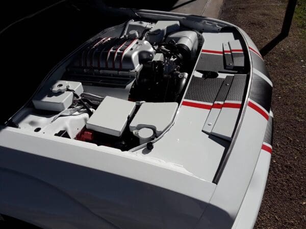A white car with a red stripe on its hood, showing an open engine compartment with visible components and parts.