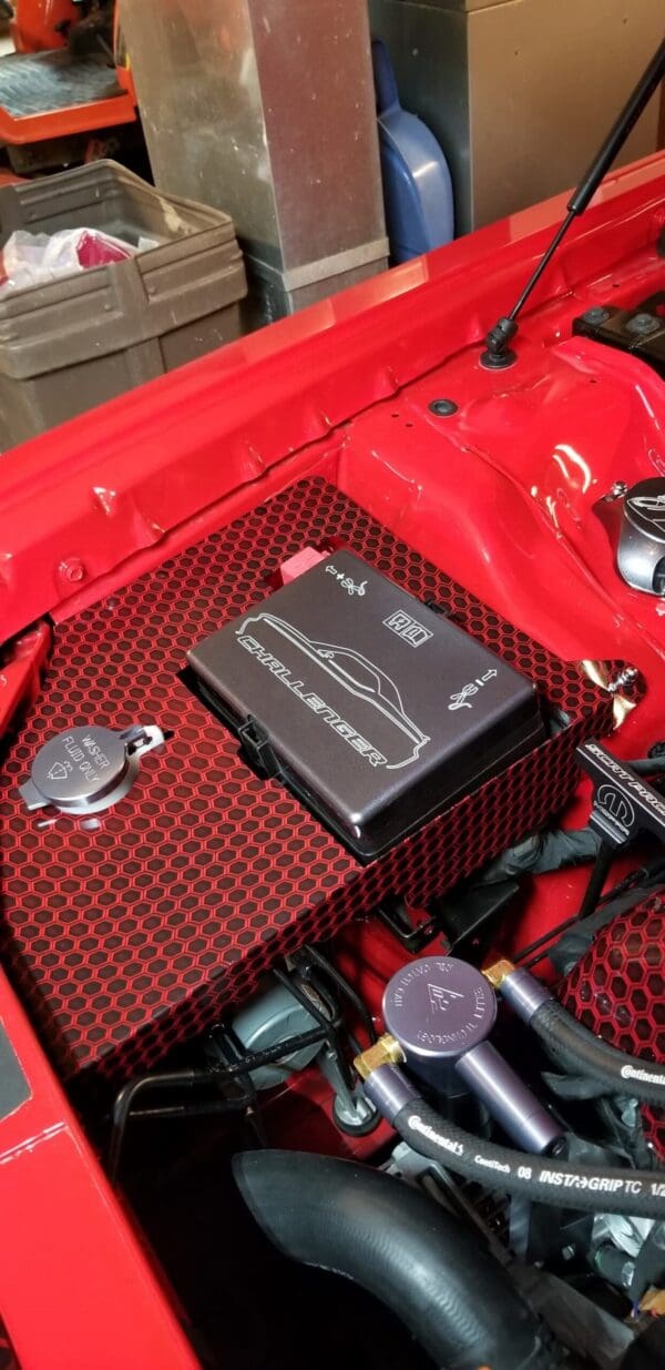 The engine compartment of a red sports car featuring a Challenger logo and various labeled components.