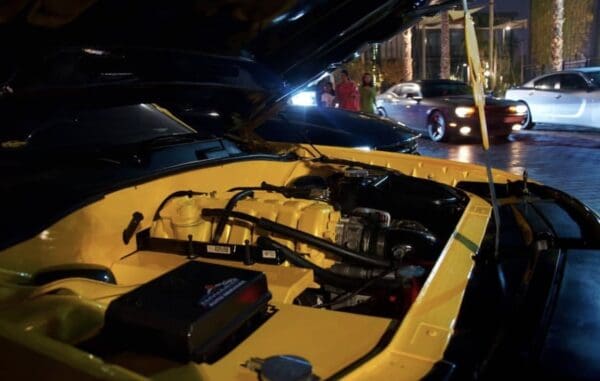 A yellow car with its hood open in a parking lot