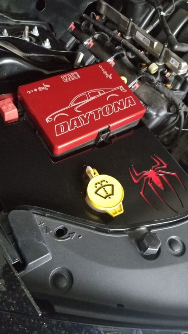 A close-up of a car engine featuring a red Daytona cover and a spider cutout.