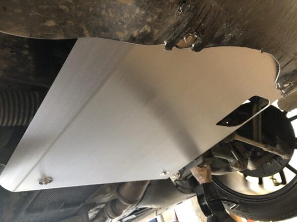 Close-up of a car's front suspension with a newly installed metal skid plate, highlighting the wheel and suspension components.