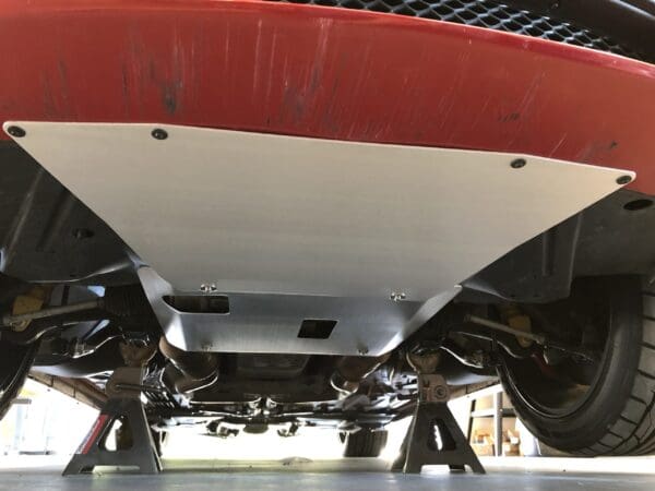 Close-up of a car's rear underside, showing the metal undercarriage and suspension, supported by jack stands.