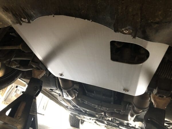 Underside view of a car with a metal skid plate installed, supported by jack stands.
