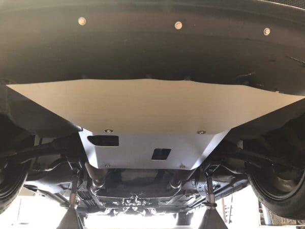 Car undercarriage with a metal skid plate, showing suspension and exhaust components, supported by jack stands.