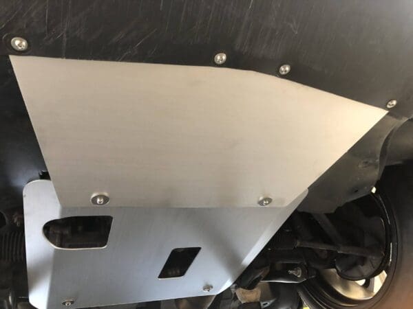 Close-up of a metallic vehicle undercarriage protector plate with visible screws and part of the wheel assembly.