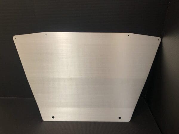 Brushed metal panel with rounded corners and drilled holes, set against a dark background.