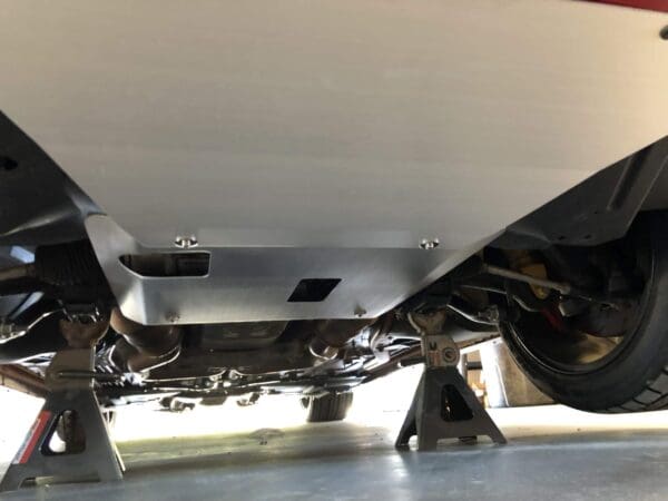 Close-up of a car's exhaust system with a metal protective panel, elevated on jack stands in a garage.