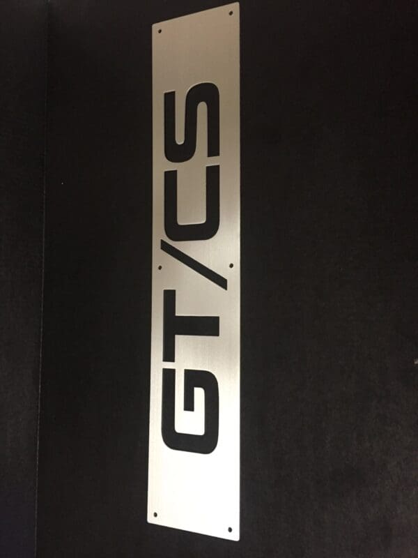 Metal informational sign with the letters 'GT/CS' on a black background.