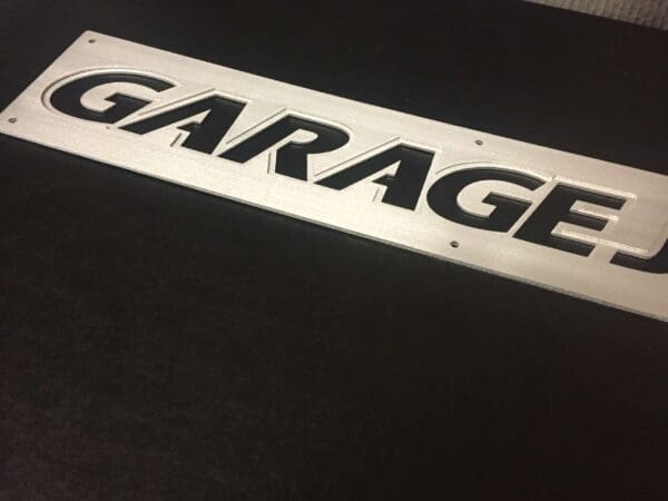 Metallic 'GARAGE' informational sign with cut-out letters on a black surface.