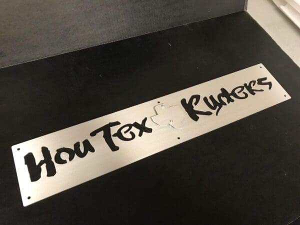 Metal informational sign with the words "HoU Tex Ruders" in a stylized font.