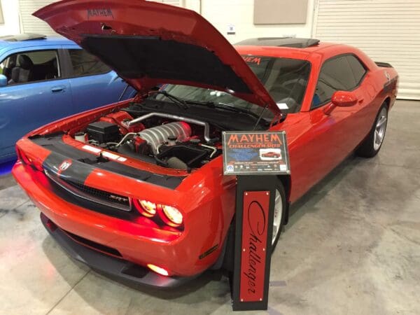 Red Dodge Challenger SRT8 with open hood displaying engine at a car show.