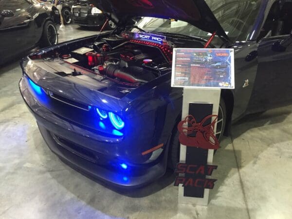 Blue Dodge Challenger with hood open displaying engine at a car show.