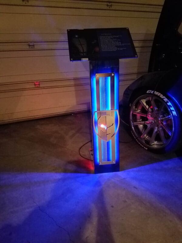 Illuminated car informatoin stand with logo next to a Corvette.