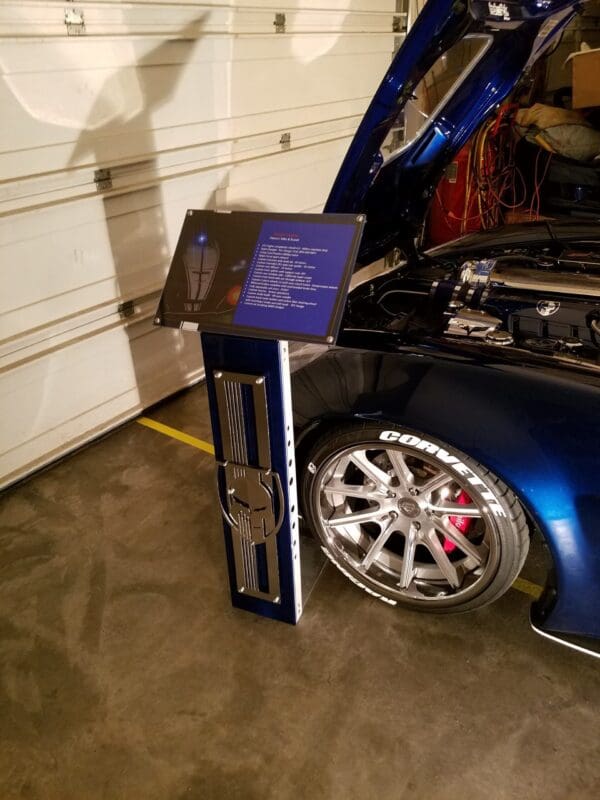 A blue car with its hood open in a garage with an information sign next to it.