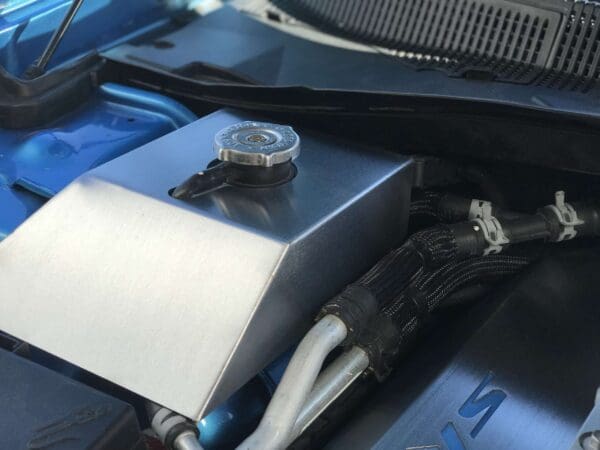 Open hood of a blue car showing the engine compartment with a metal cover and cap on a component.