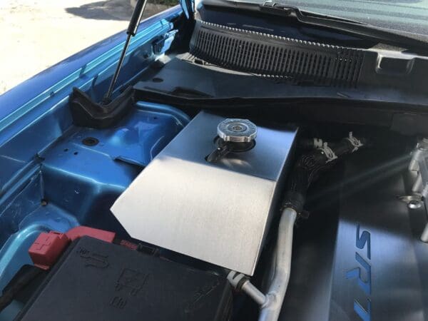 The engine compartment of a blue car with the hood open, showing various components including a metal cover and SRT branding.