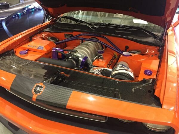 An orange Dodge sports car with its hood open, revealing a detailed engine and SRT branding.