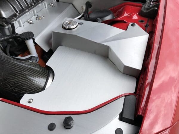 Close-up of a car engine compartment featuring metallic components, a carbon fiber intake, and a red body frame.