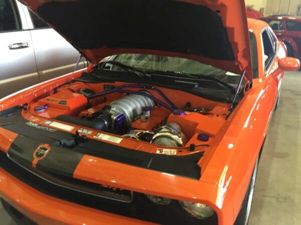 An orange car with the hood open, displaying its engine, inside a garage.