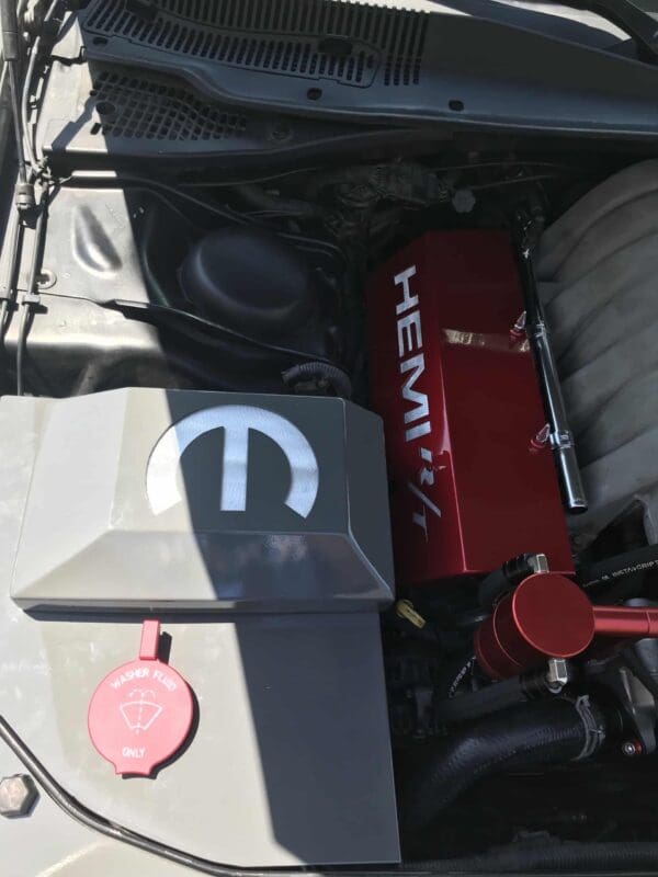 The open hood reveals a car engine compartment featuring a red HEMI cover and a red washer fluid cap.