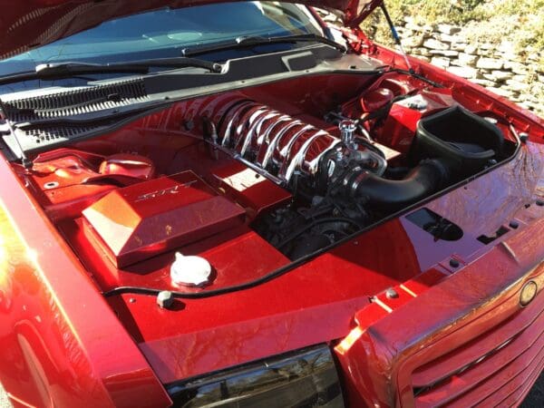 The engine of a red sports car with its hood open, showcasing the SRT branding and detailed components.