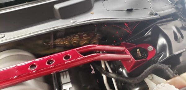 A car engine with a red strut bar and a wrench placed inside, showing various components and wiring.