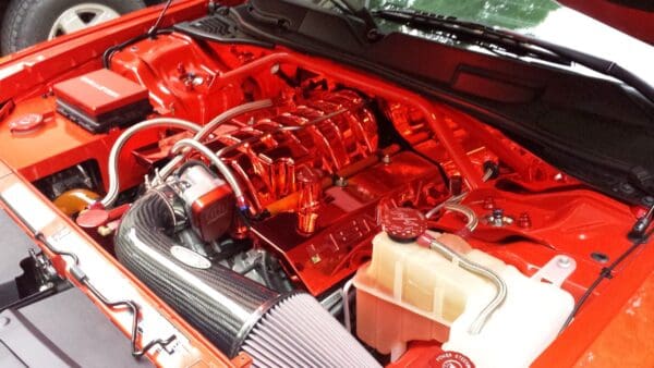 Car engine compartment with a red hood, featuring a polished chrome engine, carbon fiber air intake, and visible components.
