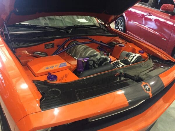 An orange sports car with its hood open, showcasing an SRT engine and custom modifications.