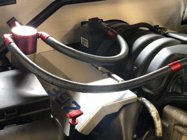 Engine close-up showing red oil catch can with hoses, part of a 392 HEMI engine setup.