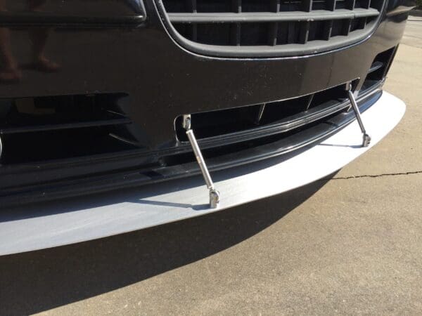 Close-up of a car's front grille with a black bumper and a silver splitter supported by metal rods.