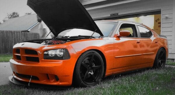 An orange car with its hood open in front of a house