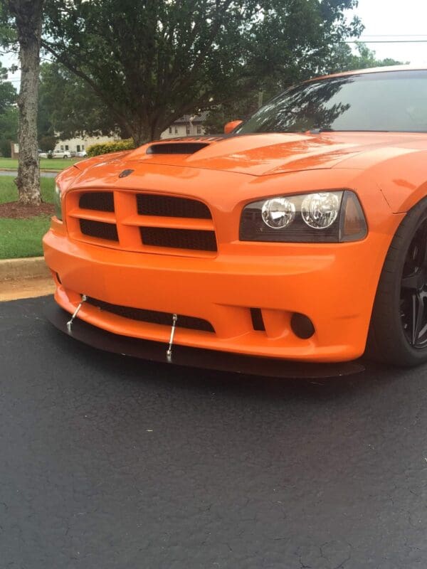 Orange Dodge Charger parked in a lot, showcasing its front grille and headlights, with trees in the background.