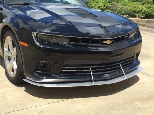 A black Chevrolet Camaro is parked in a driveway, showcasing its sleek front design and shiny exterior.