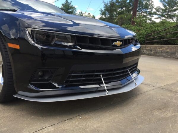 A black Chevrolet Camaro is parked in a driveway, showcasing its sleek front design and grille.