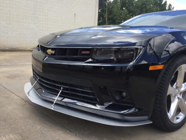 A black Chevrolet Camaro SS parked in front of a building with a white wall and trees in the background.