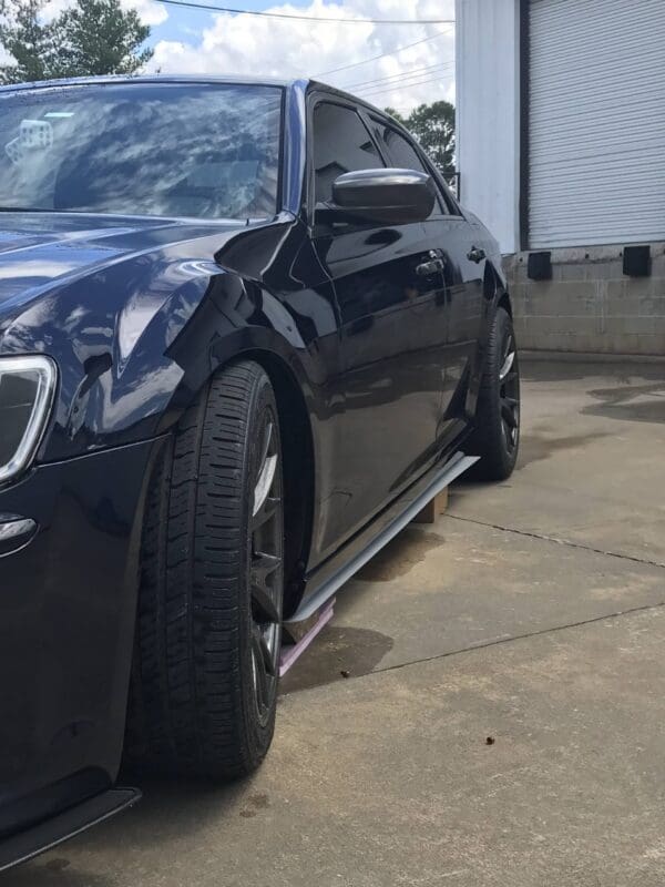 A black car with tinted windows is parked in front of a garage with a partially open door.