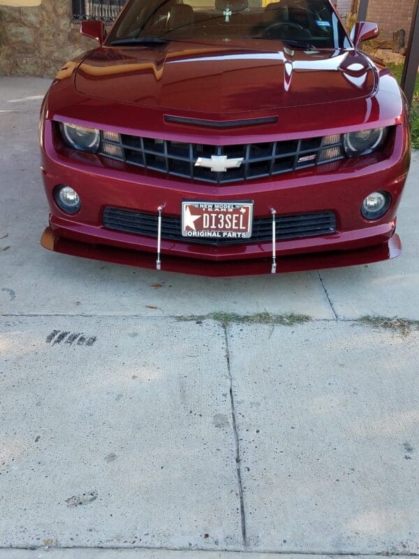 A red Chevrolet car with a license plate reading "DI3SEL" is parked in a driveway.