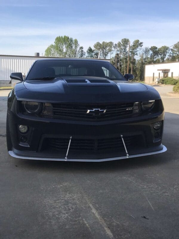 A black Chevrolet sports car parked in a lot, with trees and buildings in the background.