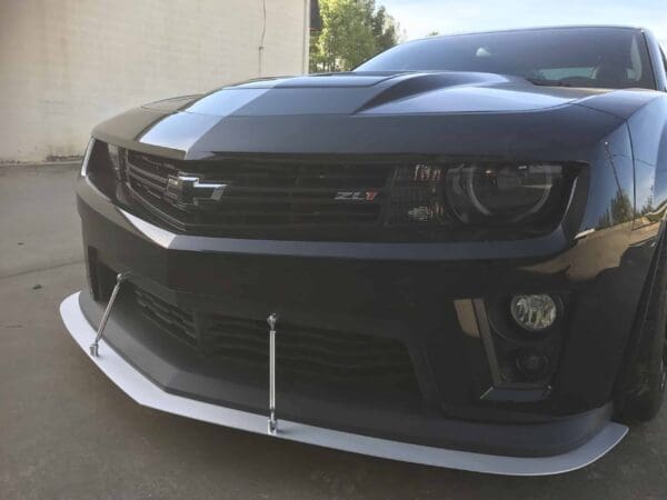 A black Chevrolet ZL1 car parked in a driveway next to a building, with a visible front splitter and badge.