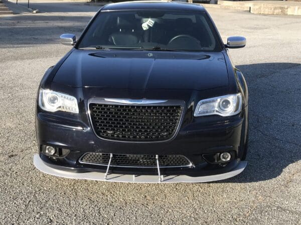 A black car with a sleek design is parked in a parking lot, featuring a prominent grille and stylish headlights.
