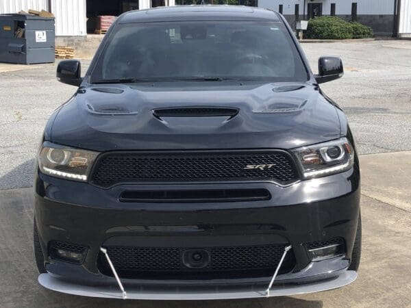 A black Dodge truck, SRT model, is parked in front of a building on a concrete surface.