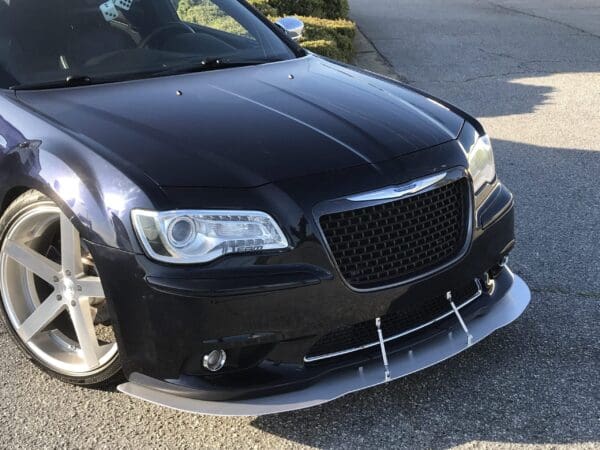 A black car with custom rims and a front splitter parked on the roadside.