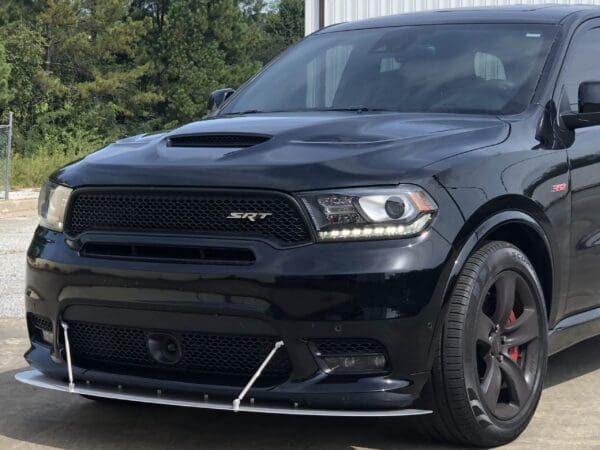 A black Dodge truck with SRT and 392 badges is parked in front of a building, surrounded by trees.
