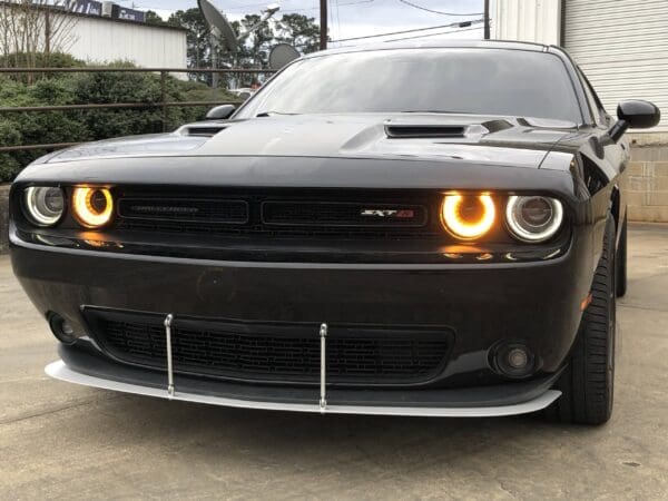 The front view of a black Dodge Challenger SXT with its headlights on, parked on a concrete surface.
