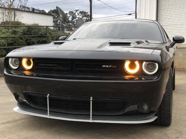 Front view of a black car with two illuminated headlights, parked outdoors.