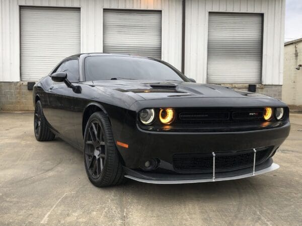 A sleek black sports car with illuminated headlights is parked in front of a building with closed garage doors.