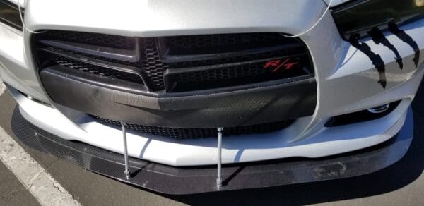 Close-up of the front of a white car, featuring a black grille, "R/T" emblem, and carbon fiber accents.