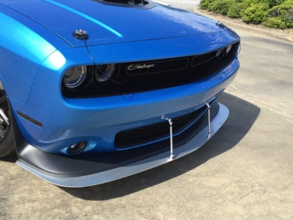 A blue Dodge Challenger parked in a lot, featuring a prominent front splitter and hood pins.